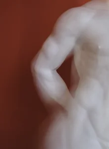 Unscharfer antiker Torso vor rotem Hintergrund, Detailaufnahme eines Arms