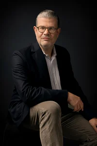 Sitzender Mann mit Brille, den Ellbogen auf dem Knie aufstützend