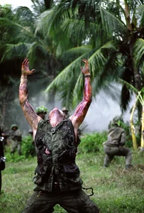 Ein Filmstill aus dem Film ‹Platoon› von Oliver Stone. Zu sehen ist ein Soldat, der auf dem Boden kniet und die Arme nach oben in den Himmel streckt.