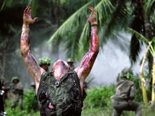 Ein Filmstill aus dem Film ‹Platoon› von Oliver Stone. Zu sehen ist ein Soldat, der auf dem Boden kniet und die Arme nach oben in den Himmel streckt.