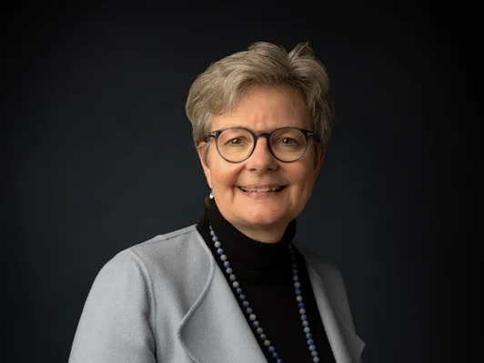 Frau mit kurzem Haar und Brille, Grauer Anzug mit schwarzem Oberteil.