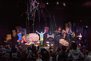 Eine Bühne mit Schauspieler*innen, Luftschlangen fliegen durch die Luft