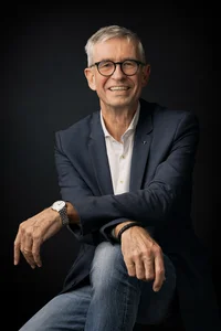 Mann mit kurzem, grauen Haar und Brille. Sitzen, die Arme auf dem Knie übereinandergelegt.
