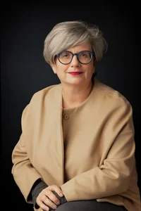 Sitzende Frau mit kurzen Haaren, mit Brille und beigem Blazer