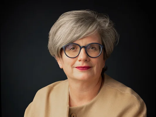Sitzende Frau mit kurzen Haaren, mit Brille und beigem Blazer
